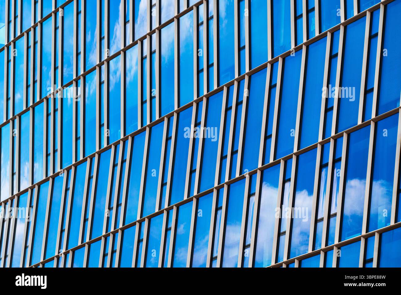Facciata riflettente in vetro blu con strisce verticali per finestre e riflessi nuvolosi Foto Stock