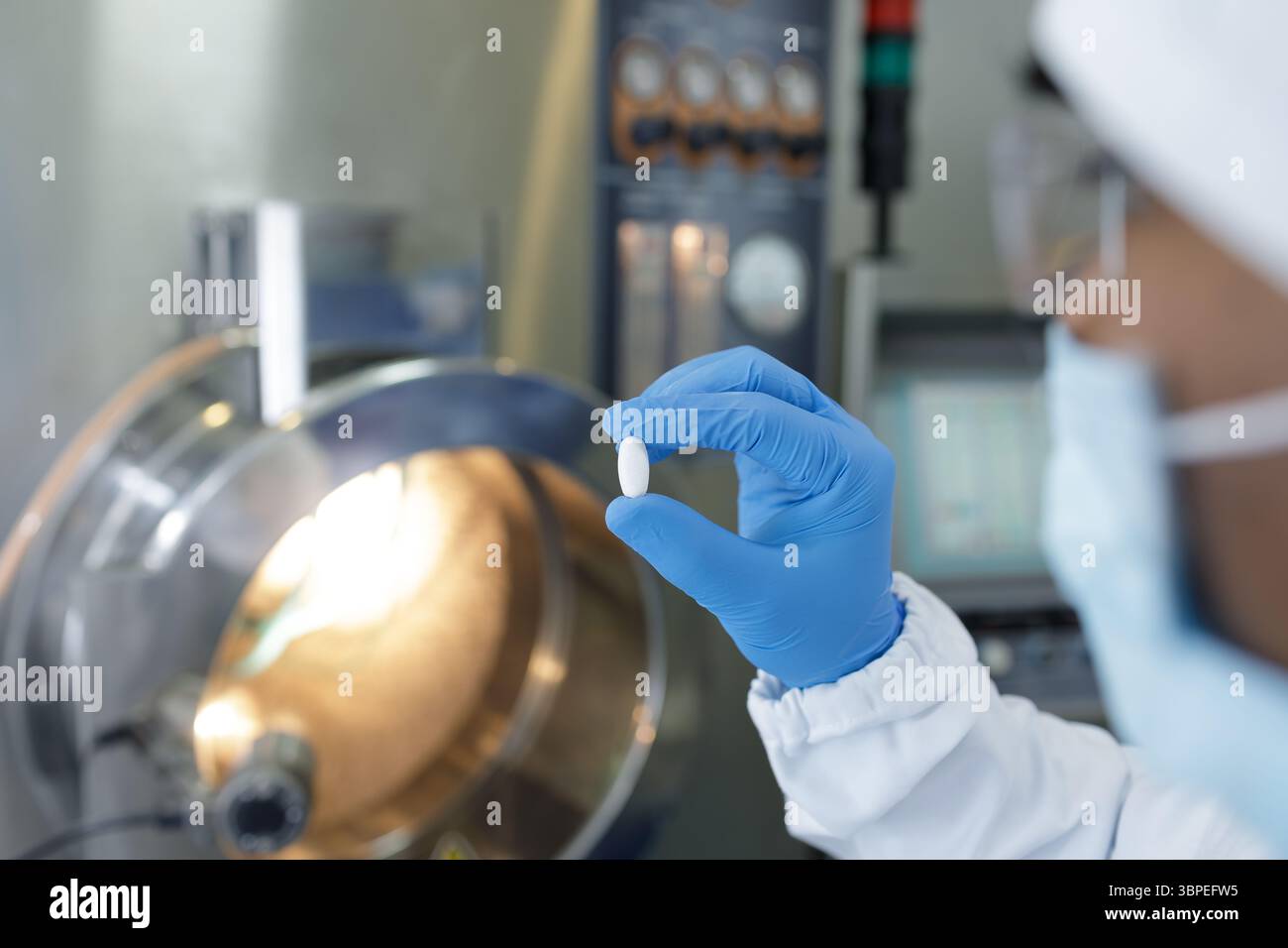 L'operatore che indossa i guanti esegue il controllo di qualità ispezionando una pillola in un impianto di produzione farmaceutica sterile Foto Stock