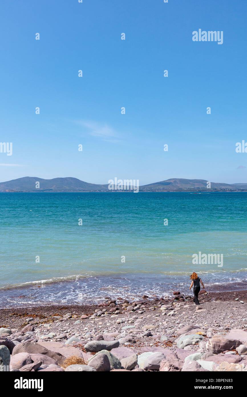 Waterville Beach, Count Kerry, Repubblica d'Irlanda: Affacciata sulla baia di Ballinskelligs. Una bella giornata di sole. Una donna solitaria passeggia fino al bordo delle acque Foto Stock