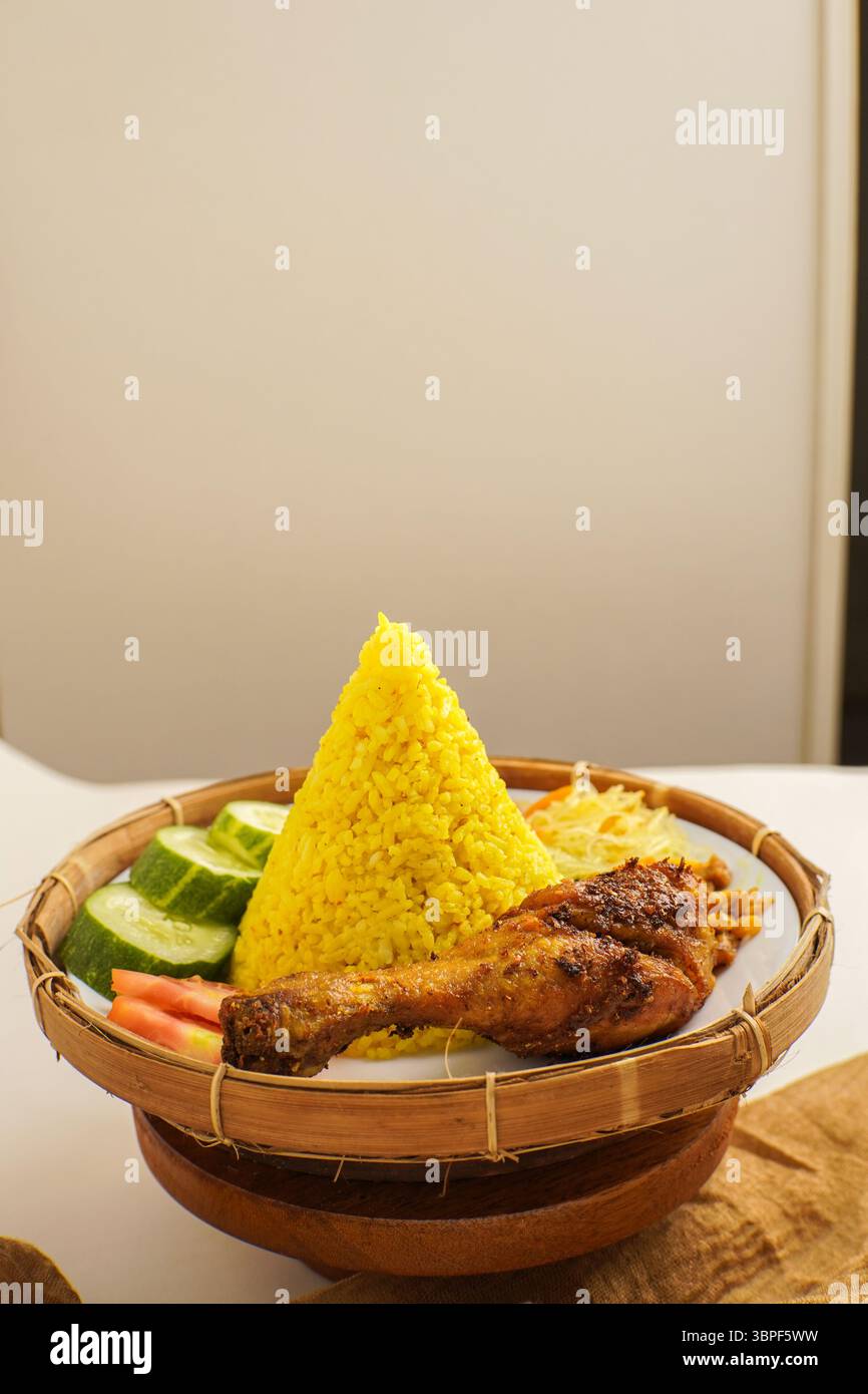 Vista dall'alto del tradizionale riso giallo indonesiano con sambal, tempeh, spaghetti e verdure servite su un piatto. Foto Stock