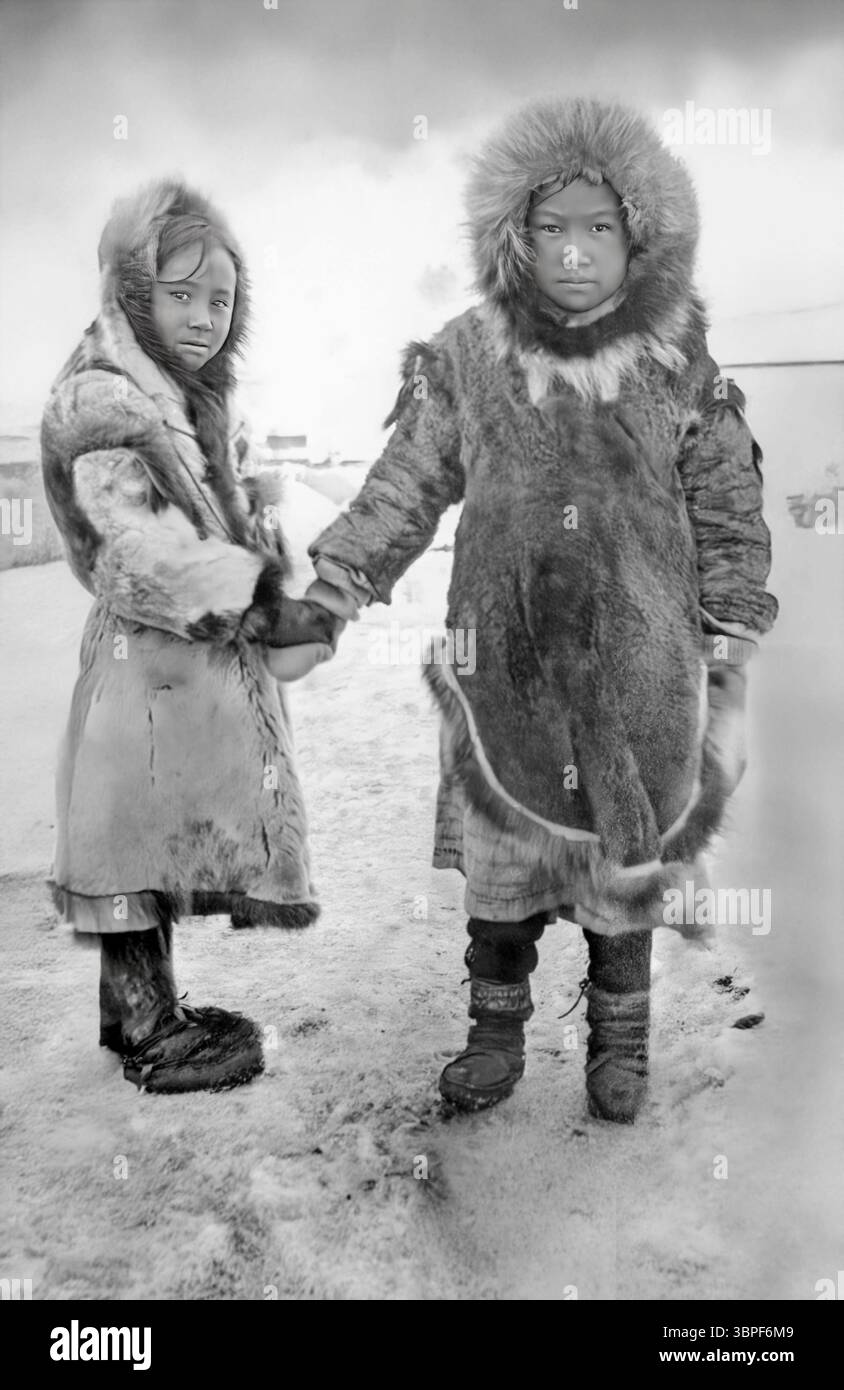 Due ragazze Inuit che stringono le mani, vestite con abiti indigeni a nome, Alaska. Nel 1900, influenze esterne (come missionari, commercianti e politiche governative degli Stati Uniti) cominciarono ad avere un impatto sulla vita Inuit, specialmente negli insediamenti costieri come nome. Ciò includeva: Pressione per adottare abbigliamento occidentale e cristianesimo Introduzione di collegi che separavano i bambini dalla loro cultura declina nella lingua e nelle usanze tradizionali in alcune aree nonostante queste pressioni, le ragazze Inuit hanno svolto un ruolo vitale nel mantenere la conoscenza culturale, garantendo la sopravvivenza del loro popolo Foto Stock