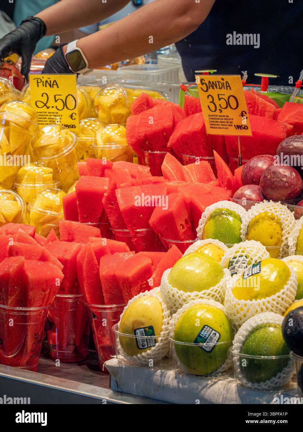 Coppette di frutta fresca tagliate, tra cui anguria (sandía) e ananas (piña), in vendita presso un colorato chiosco del mercato la Boqueria, Barcellona, Spagna. Foto Stock