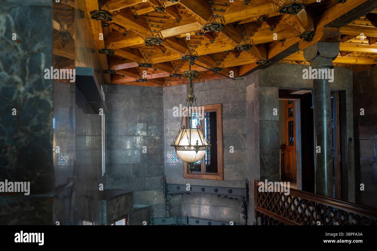 Una storica lampada decorata è appesa all'intricato soffitto a cassettoni in legno nell'interno Art Nouveau del Palau Güell di Antoni Gaudí, Barcellona, Spagna. Foto Stock