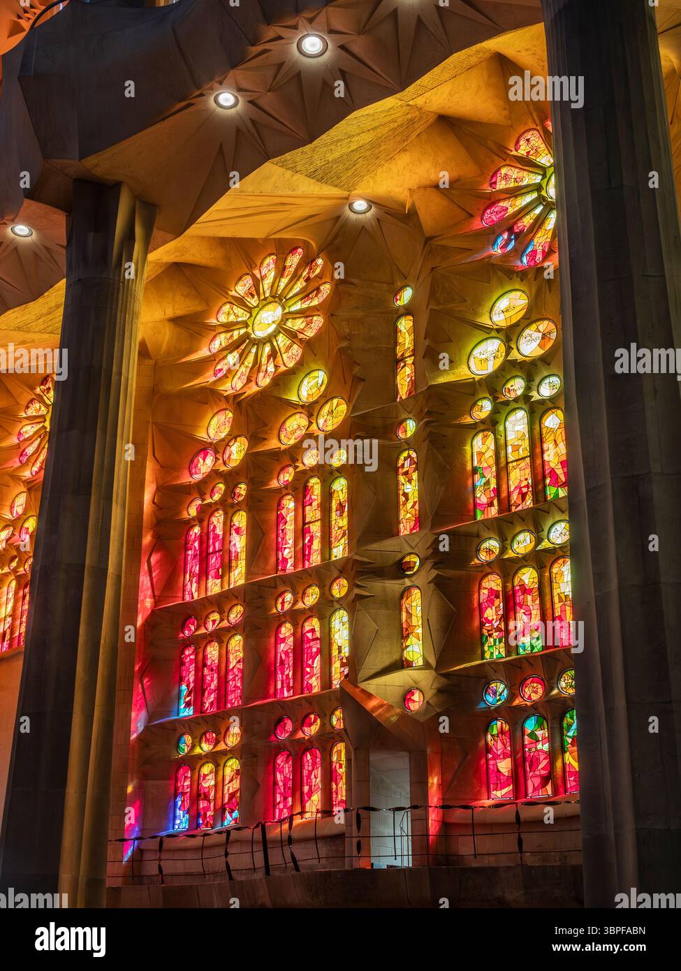 Luce rossa e arancione dalle vetrate colorate illuminano le colonne e i soffitti a volta della Sagrada Familia, Barcellona, Spagna. Foto Stock