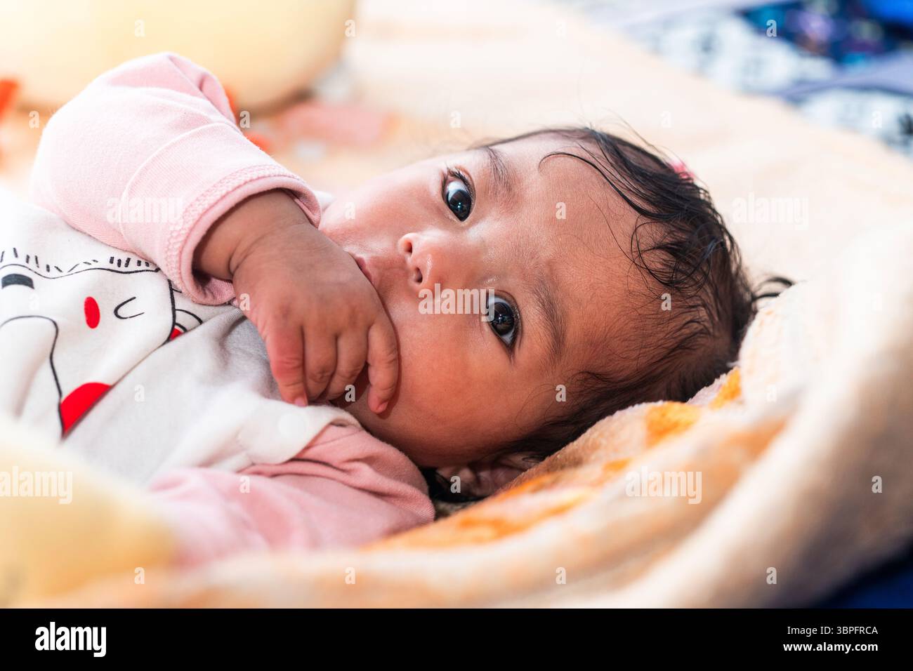 Un simpatico bambino indonesiano in abiti caldi adagiato su una coperta colorata Foto Stock