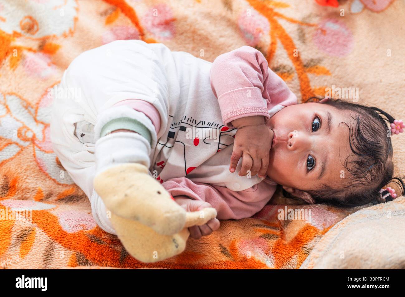 Un simpatico bambino indonesiano in abiti caldi adagiato su una coperta colorata Foto Stock
