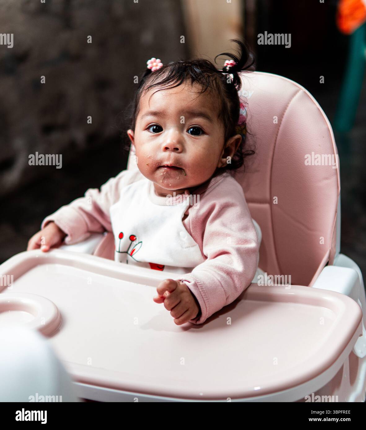 Una bambina siede su un seggiolone a casa in Indonesia, mostrando la vita quotidiana della famiglia. Foto Stock