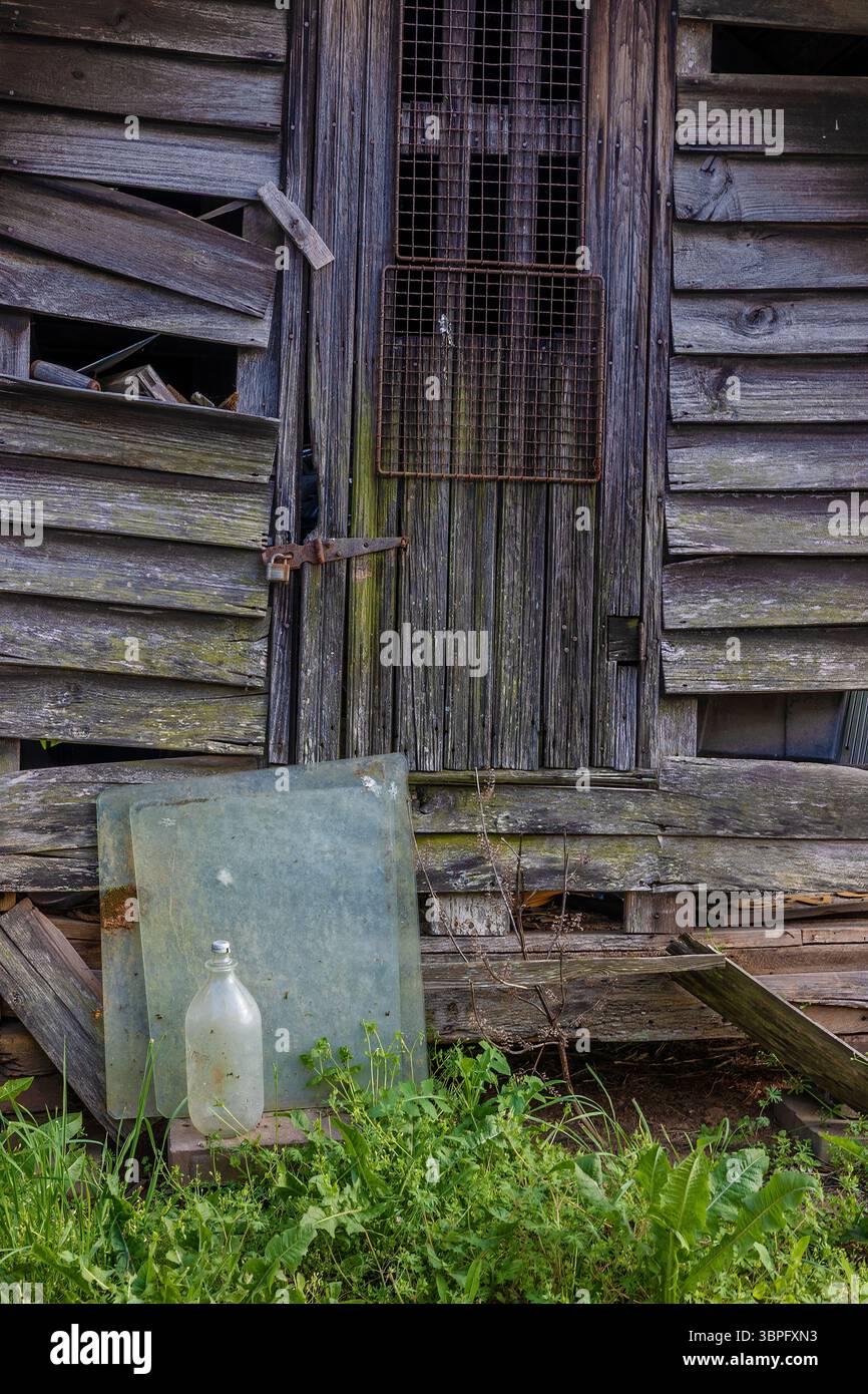 Vecchio edificio in decadenza con quadrati di vetri e una vecchia bottiglia seduta vicino alla porta. Foto Stock