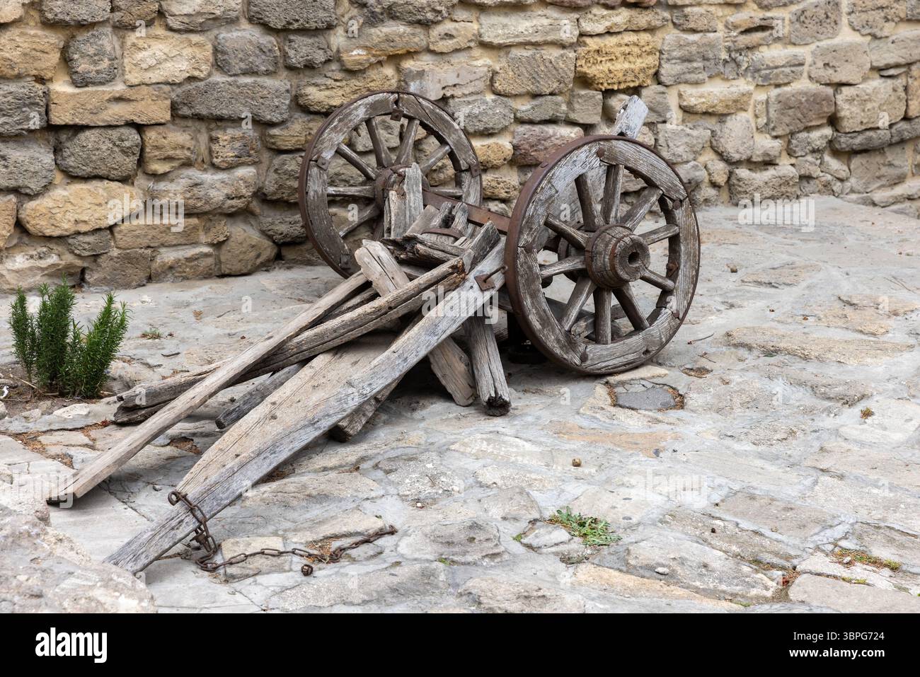 Ruote rustiche in legno e un telaio in legno si appoggiano su un muro di pietra, trasudando fascino storico e un'estetica vintage in un tranquillo setti all'aperto Foto Stock