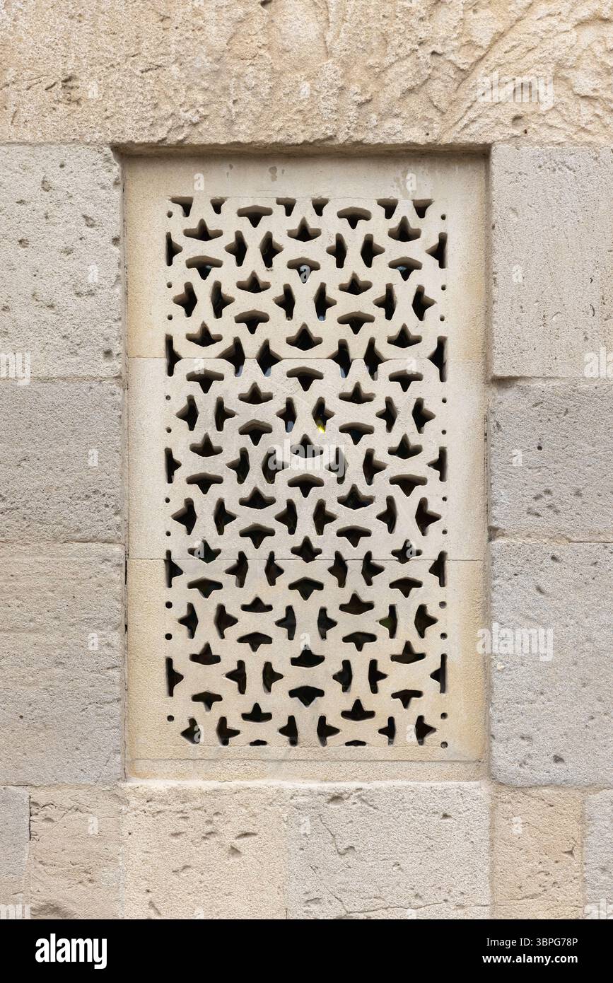 Lavorazioni in pietra intagliate con un design geometrico traforato incastonato in un muro rustico, a dimostrazione della maestria architettonica e della tradizione Foto Stock