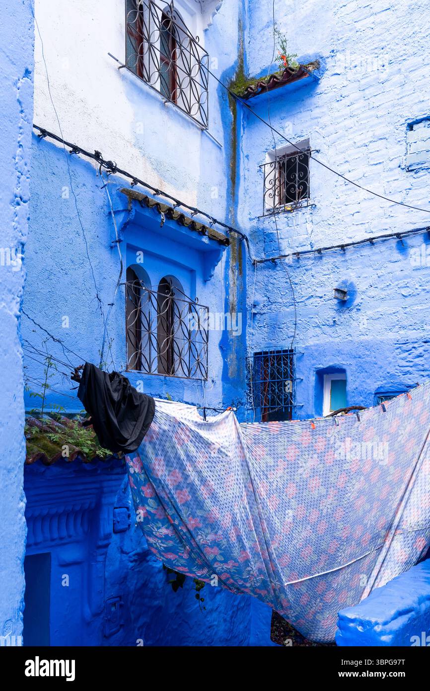 Chefchaouen, Marocco - 26 marzo 2024: Abiti che si asciugano tra le case completamente blu di Chefchaouen in Marocco durante una giornata nuvolosa Foto Stock