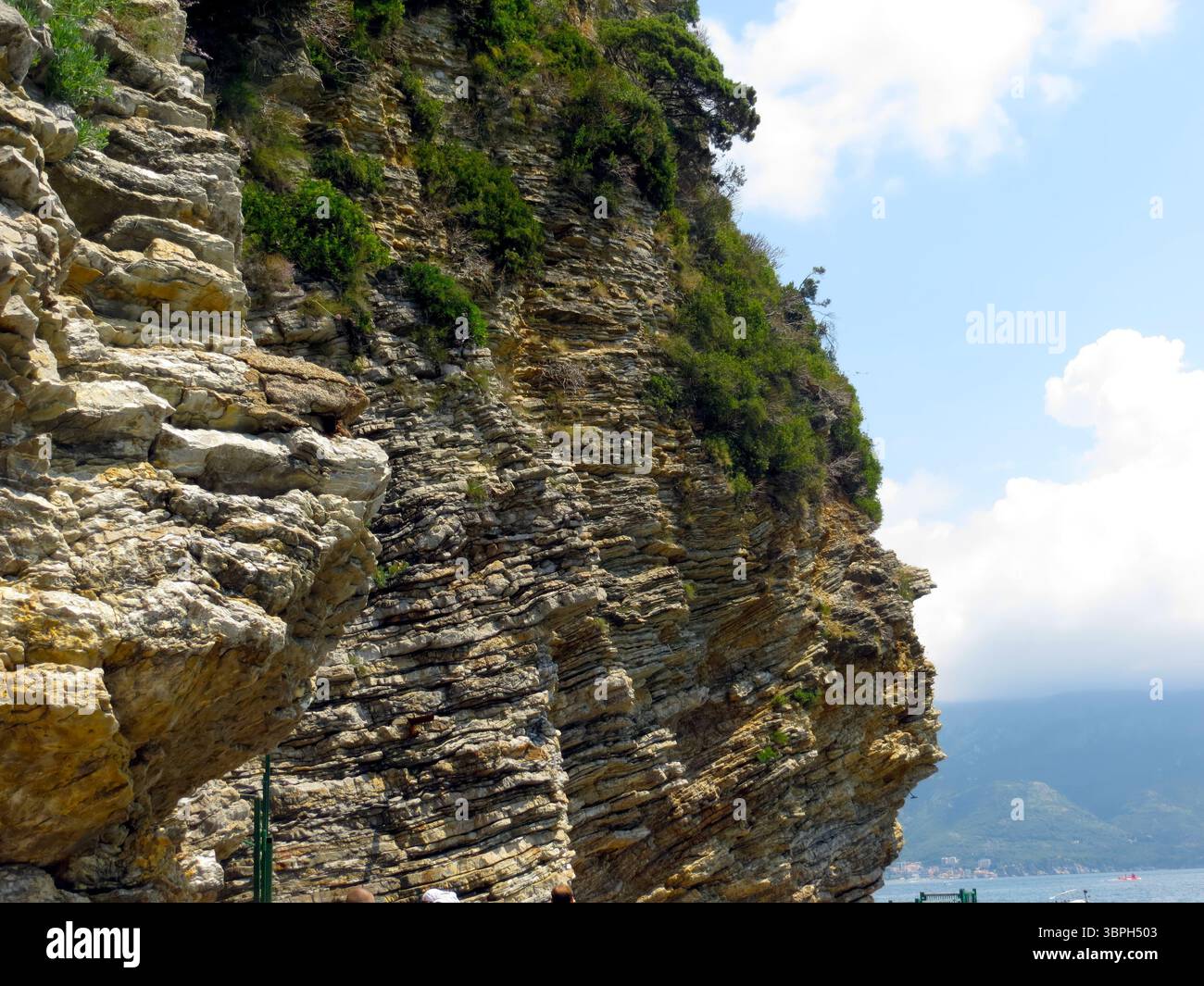 Le maestose scogliere rocciose si innalzano drammaticamente dalla costa del Montenegro, circondate da una vegetazione lussureggiante e da cieli azzurri. I visitatori apprezzano la natura Foto Stock