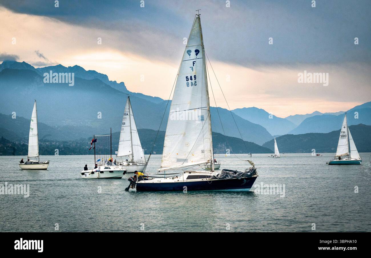 In tarda giornata, barche a vela sul lago di Annecy, nella foresta alpina delle alpi con case, chiese e hotel che punteggiano l'ecoregione delle foreste miste delle Alpi Foto Stock