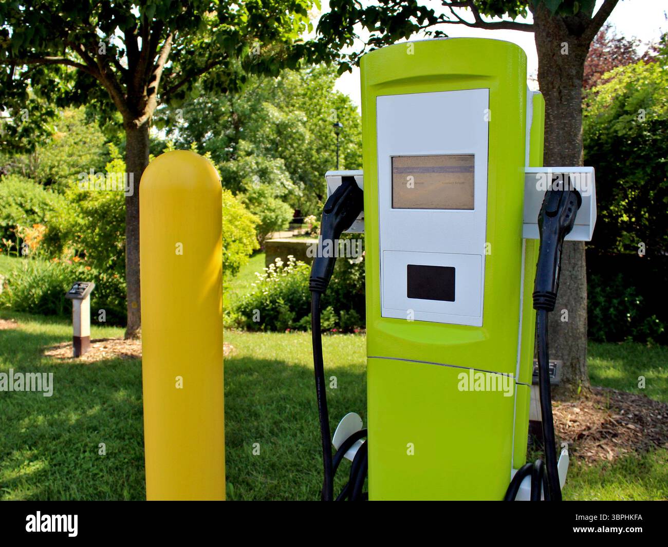 Una moderna stazione di ricarica per veicoli elettrici si fonde in un vivace paesaggio verde, simboleggiando il futuro pulito e tranquillo dei trasporti sostenibili. Foto Stock