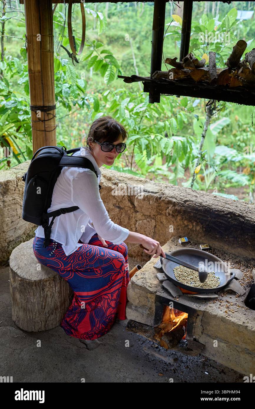 Donna che mescola i chicchi di caffè verde in una tradizionale teglia da torrefazione Foto Stock