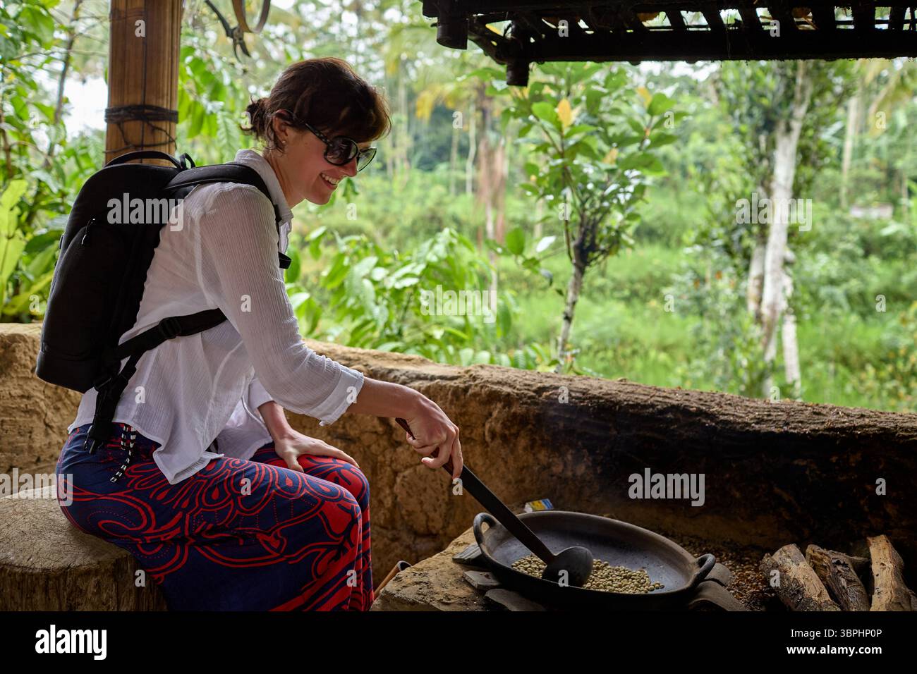 Donna sorridente mentre tosta i chicchi di caffè verdi in modo tradizionale Foto Stock