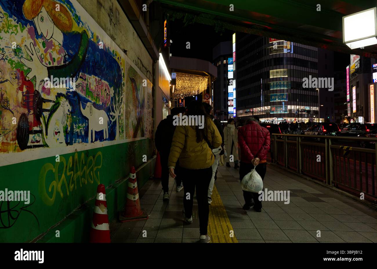 Persone che camminano lungo un marciapiede murale di Tokyo di notte con luci della città, traffico e edifici illuminati sullo sfondo Foto Stock