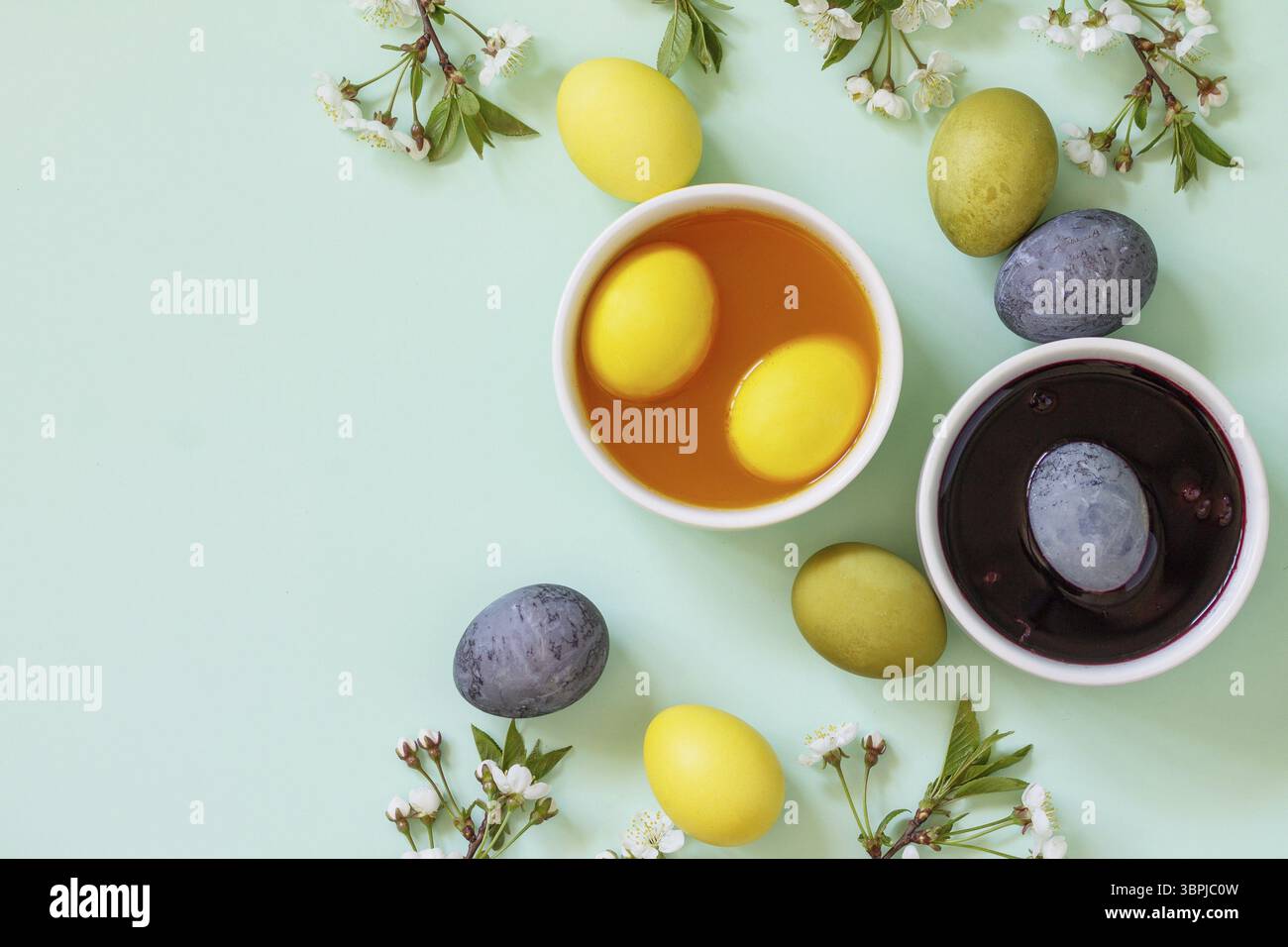 Colorante naturale per uova di pasqua - carcato e curcuma. Uova di pasqua colorate fatte in casa su sfondo verde chiaro. Vista dall'alto, disposizione piatta. Copia spazio Foto Stock
