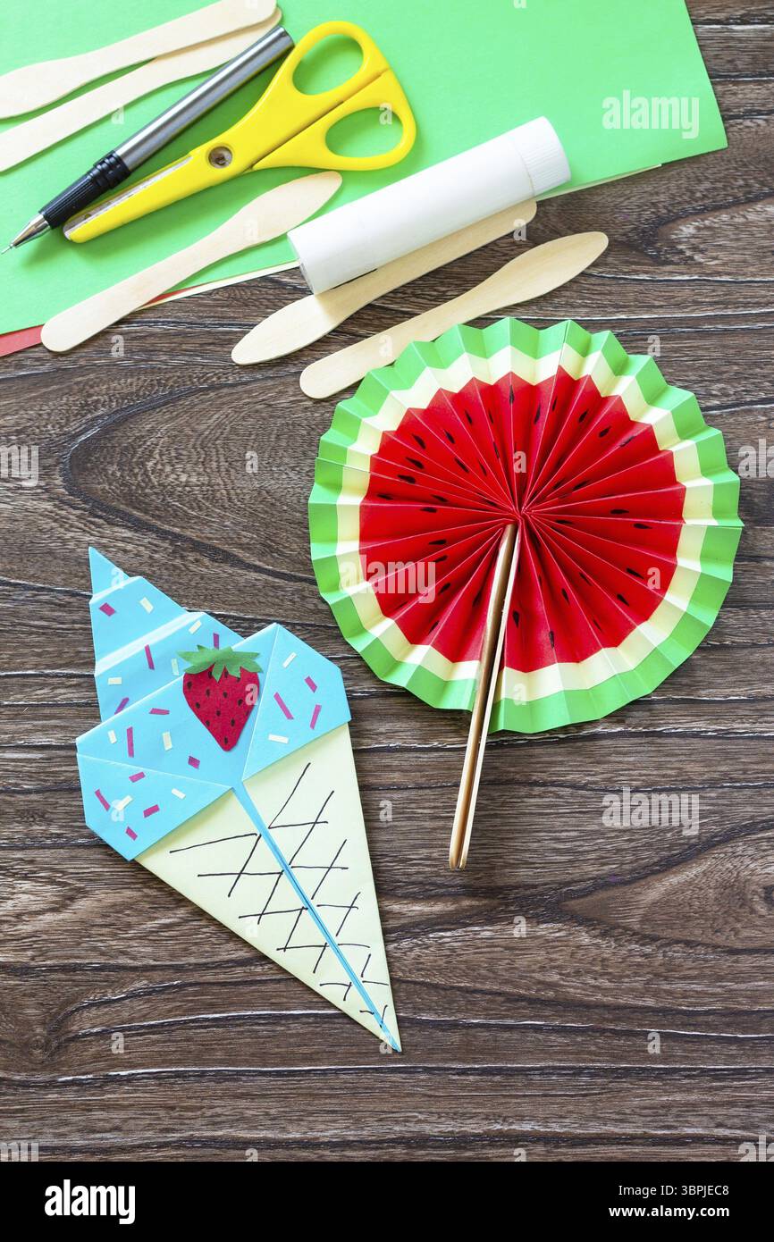 Anguria del ventilatore di carta e gelato di carta origami, bastoncini di legno del giocattolo estivo su un tavolo di legno. Progetto artistico per bambini, fatto a mano, artigianato per bambini Foto Stock