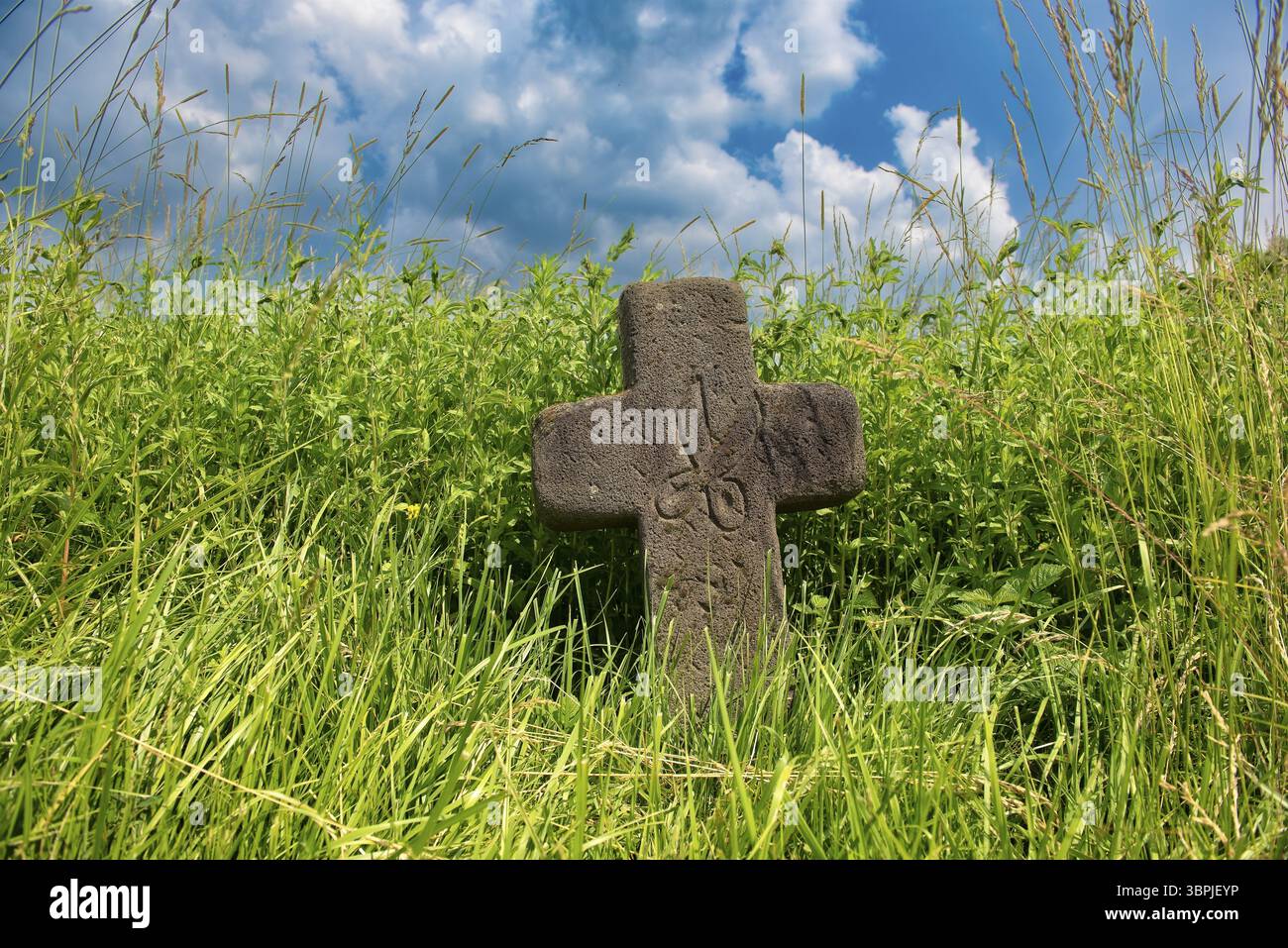 Una pietra commemorativa in arenaria a forma di croce con forbici cesellate sul bordo del sentiero in un campo Foto Stock