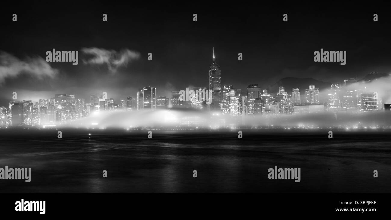 Una notte nebbiosa al Victoria Harbour di Hong Kong, caratterizzato da un suggestivo paesaggio urbano bianco e nero con grattacieli parzialmente oscurati dalla nebbia. Foto Stock