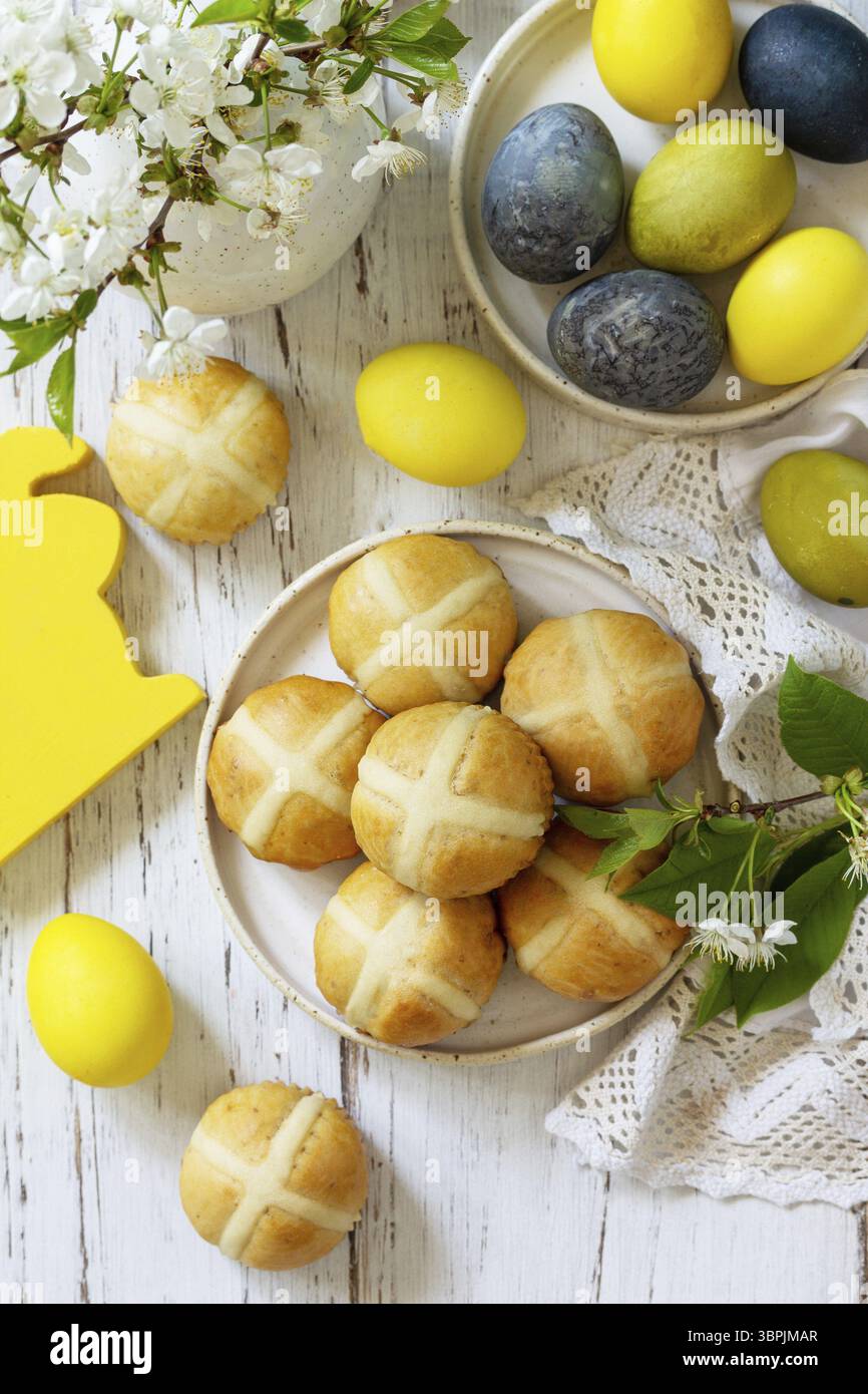 Felice Pasqua cibo festivo concetto. Tradizionale croci pasquali caldi fatti in casa con uva passa e uova pasquali colorate naturali su un tavolo rustico. Vista dall'alto Foto Stock Felice Pasqua cibo festivo concetto. Tradizionale croci pasquali caldi fatti in casa con uva passa e uova pasquali colorate naturali su un tavolo rustico. Vista dall'alto Foto Stock