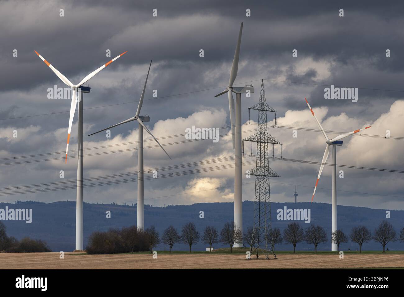 Turbine eoliche di una centrale eolica in un teleobiettivo condensato con montagne all'orizzonte e copertura nuvolosa grigia chiusa Foto Stock