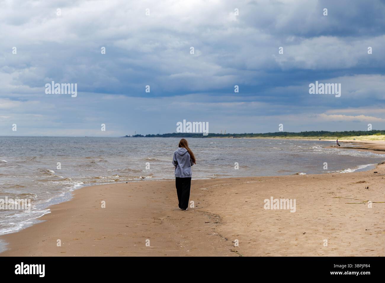 paesaggio di spiaggia, un uomo si erge su una spiaggia sabbiosa, guardando il vasto mare sotto un cielo nuvoloso, con una spiaggia Foto Stock