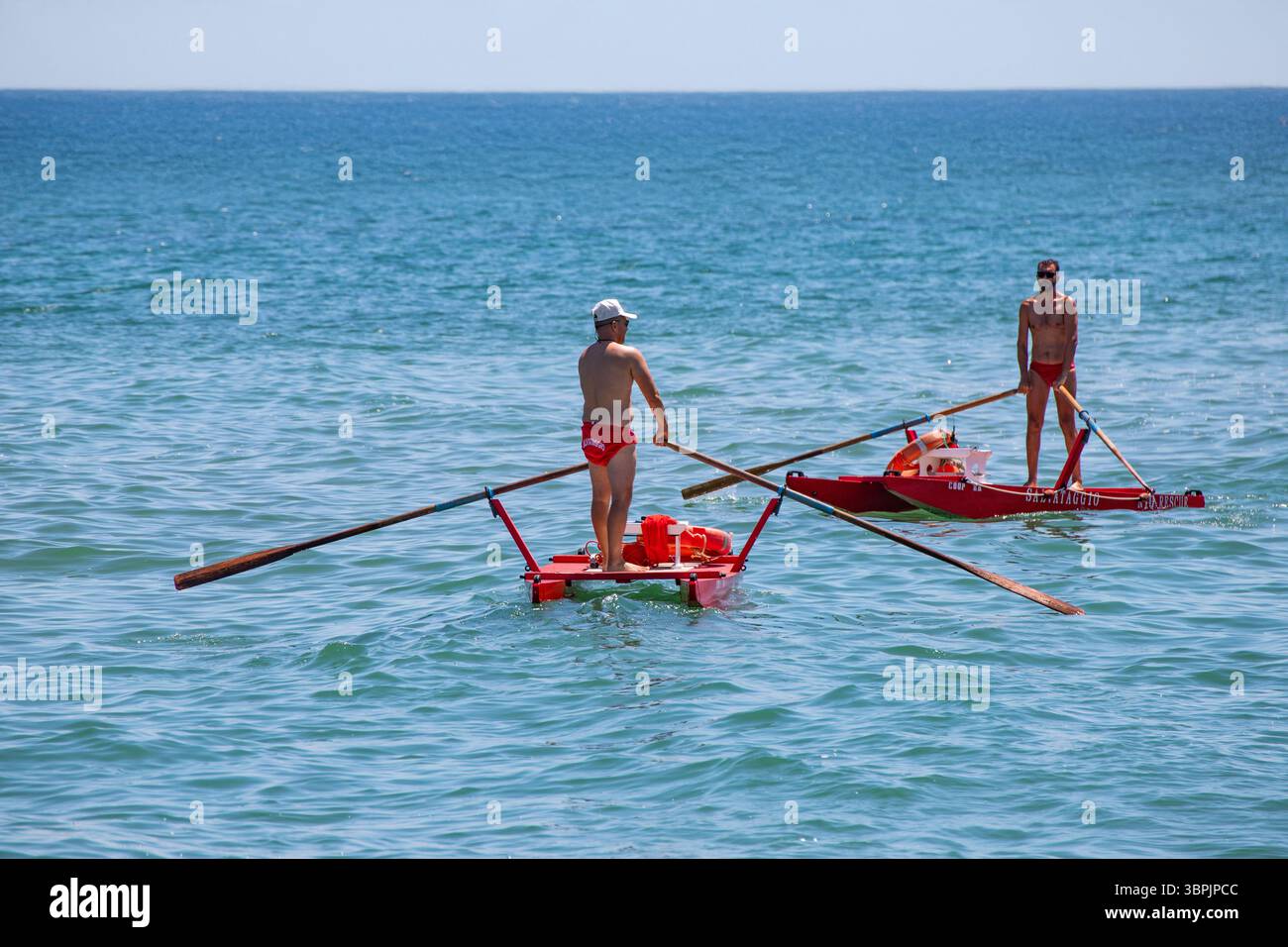 Il bagnino dimostra forza e urgenza mentre rema la sua nave verso una potenziale vittima annegante. Un vero eroe in mare. Foto Stock