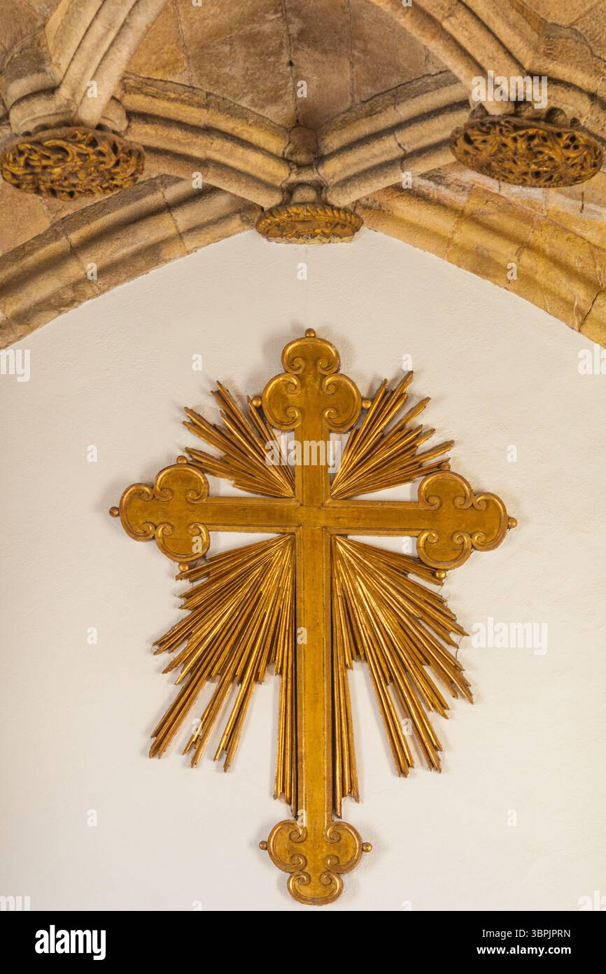 Una radiosa croce dorata con raggi intricati e dettagli ornati, montata su un arco in pietra, che simboleggia il significato religioso Foto Stock