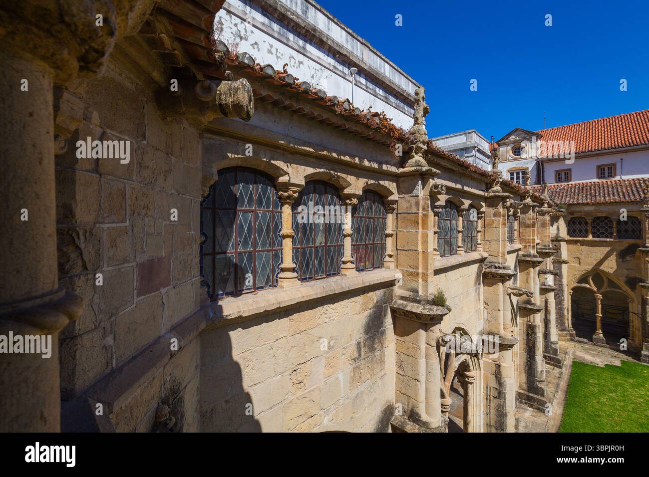 Un edificio storico in pietra con finestre ad arco, intricati lavori in pietra e un tetto piastrellato, adagiato su un cielo blu luminoso, che mostra un'architettura senza tempo Foto Stock