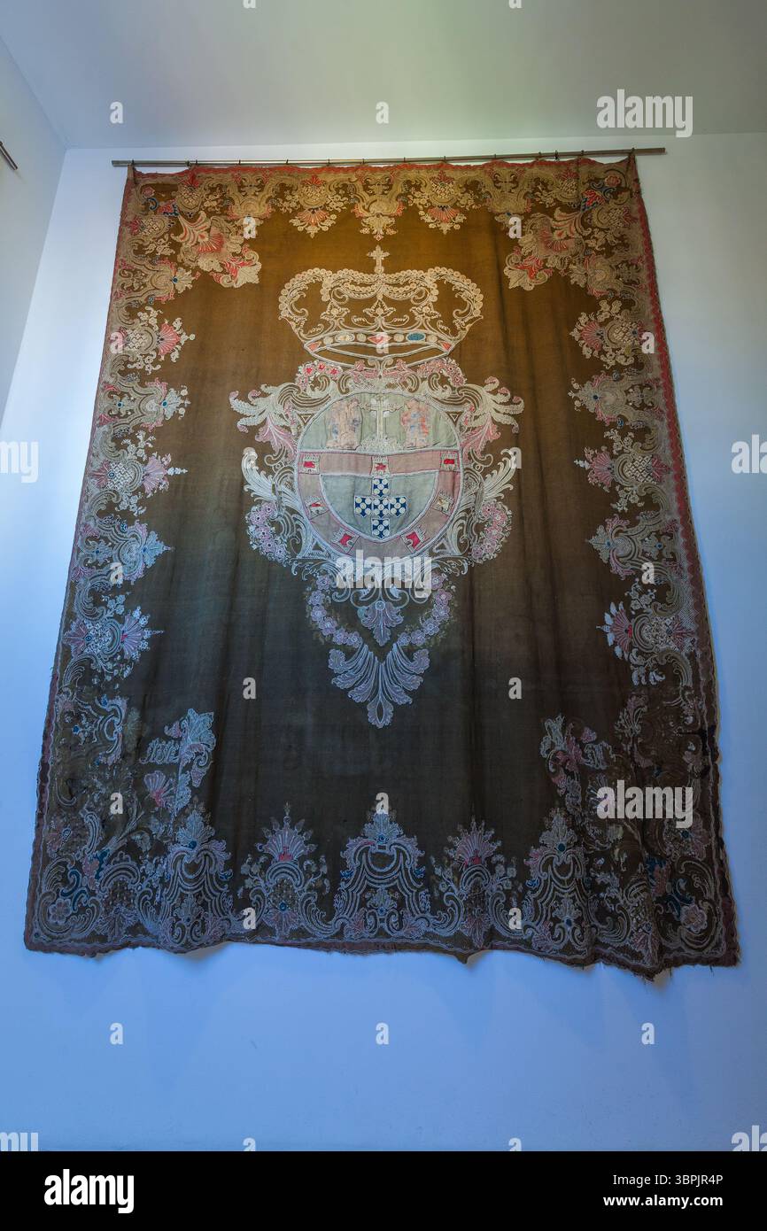 Un tappeto ricamato con uno stemma centrale con una corona, circondato da intricati motivi floreali e araldici su sfondo scuro Foto Stock
