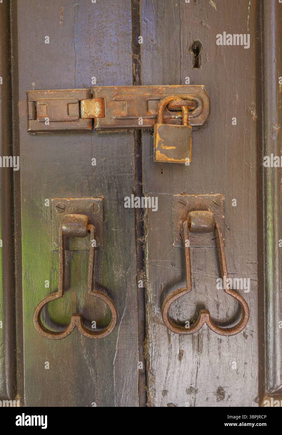 Una porta in legno con elementi in metallo rustico, tra cui una serratura, un lucchetto e maniglie ornate, che mostrano segni di età e di utilizzo Foto Stock