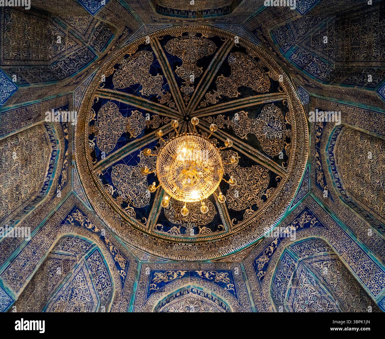 Una splendida vista di una cupola dal design complesso caratterizzata da motivi ornati blu e oro, con un lampadario centrale che illumina lo spazio. Foto Stock