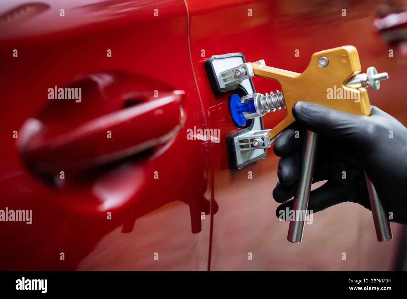 attrezzo di riparazione ammaccature per auto senza verniciatura. Uomo che fissa la portiera rossa del veicolo con tecnologia PDR Foto Stock