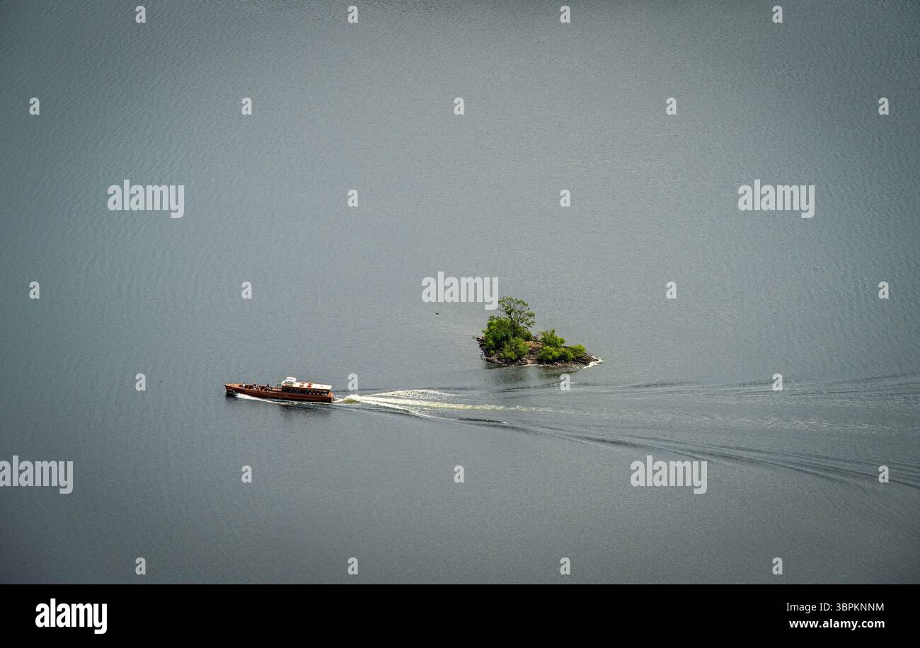 Vista aerea di un traghetto che vola sulla tranquilla superficie del lago Derwentwater, passando vicino a una piccola isola e lasciandosi alle spalle un dolce sentiero d'acqua Foto Stock