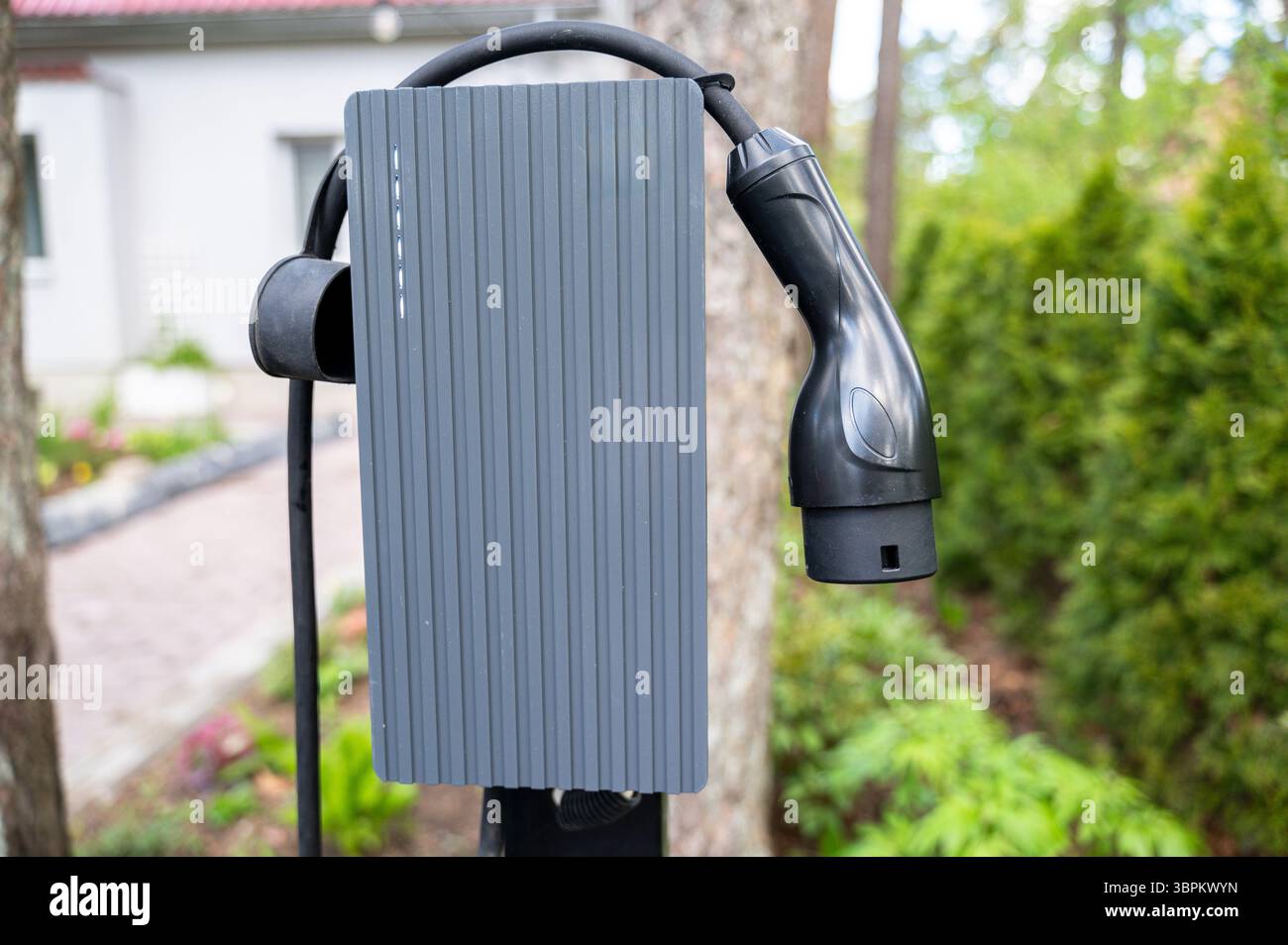 Vista ravvicinata del caricabatteria per auto elettrico montato all'esterno nel vialetto di casa. La configurazione riflette l'impegno per l'energia pulita e il pratico chargin personale Foto Stock
