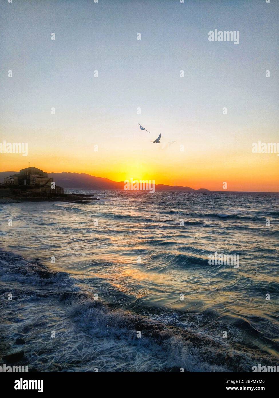 Tramonto sul mare con due uccelli che volano vicino alla costa rocciosa di Creta, in Grecia, catturando una tranquilla scena serale mediterranea. Foto Stock