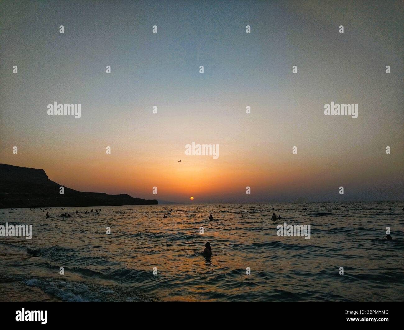 Tramonto sul mare con persone che nuotano e scogliere sagomate sulla costa di Creta, una serena scena serale nelle acque mediterranee della Grecia. Foto Stock