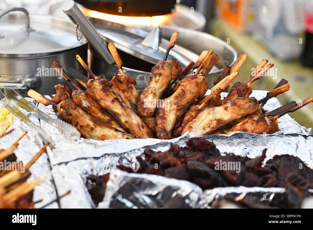 Spiedini di pollo tailandese alla griglia in mostra al mercato del cibo di strada. Tradizionale gai yang con bastoni di legno Foto Stock