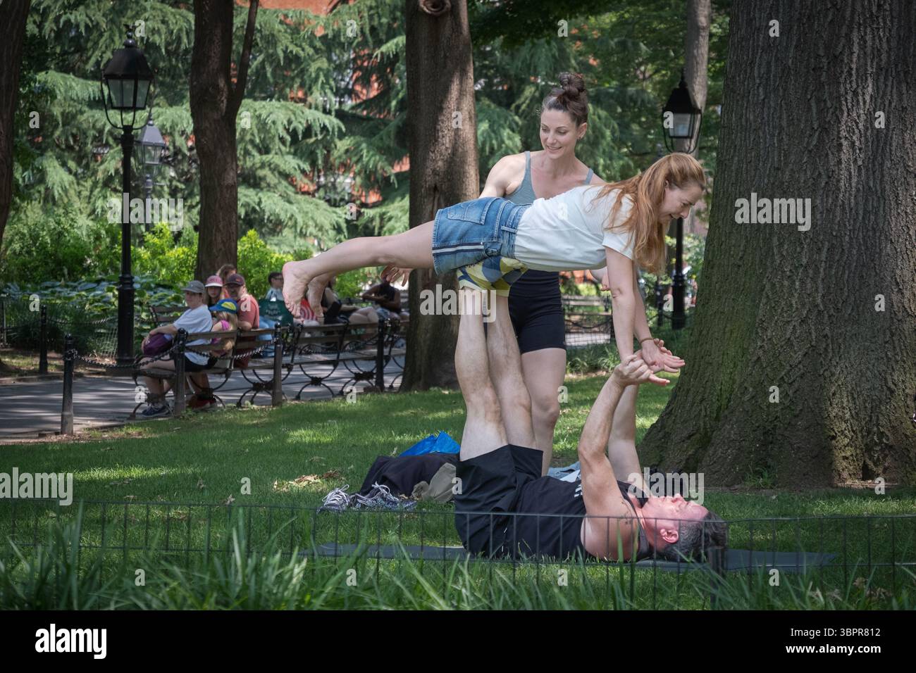 2 esperti e ambasciatori di Acroyoga mostrano a una donna vicina una posizione di base. Al Washington Square Park di Manhattan, New York. Foto Stock