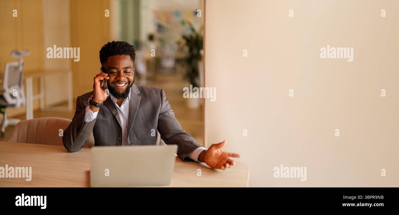 Un professionista di sesso maschile felice con un laptop sulla scrivania che discute le strategie aziendali tramite telefono cellulare in ufficio Foto Stock