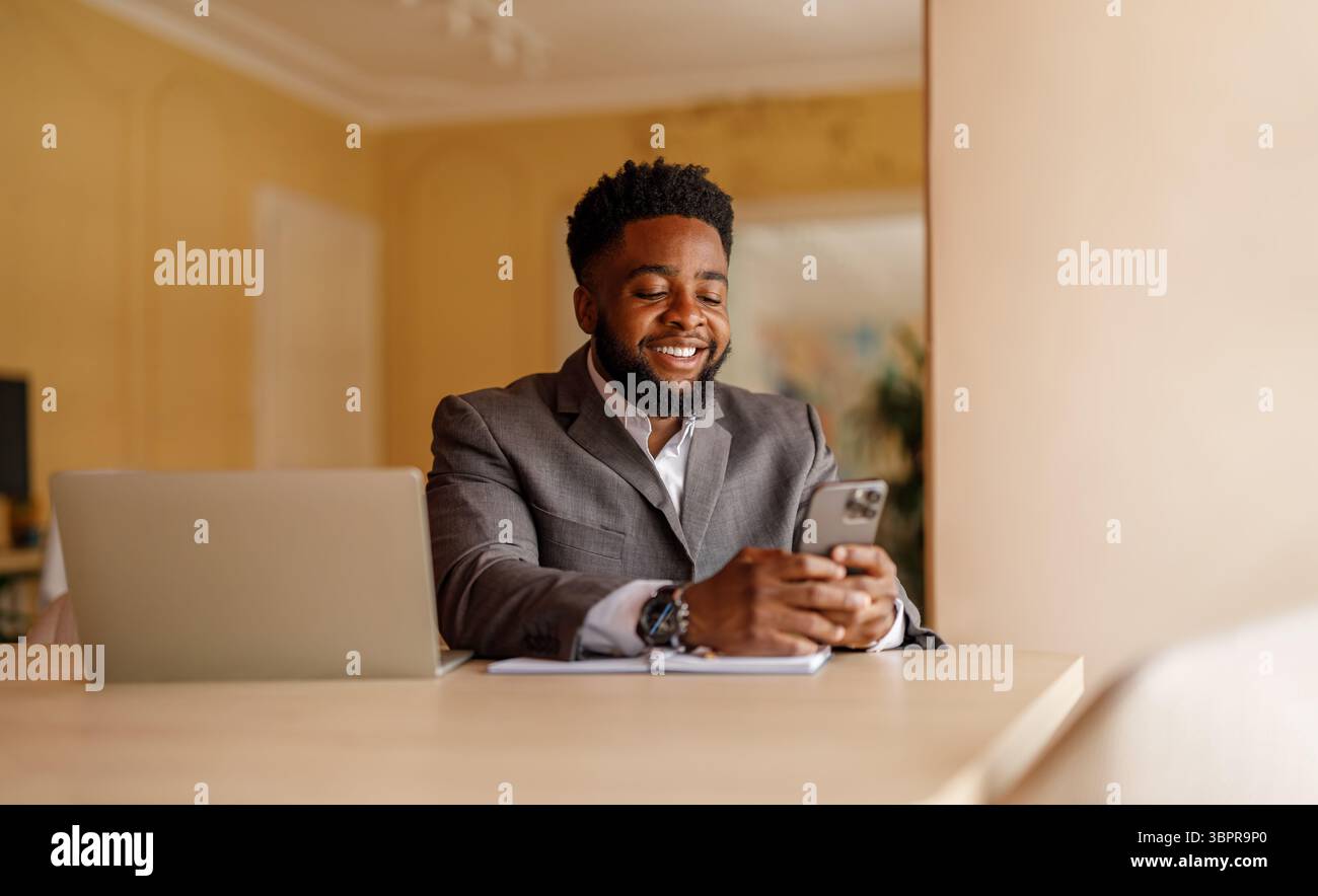 Ritratto di un uomo d'affari sorridente che utilizza applicazioni online su smartphone mentre lavora in ufficio Foto Stock
