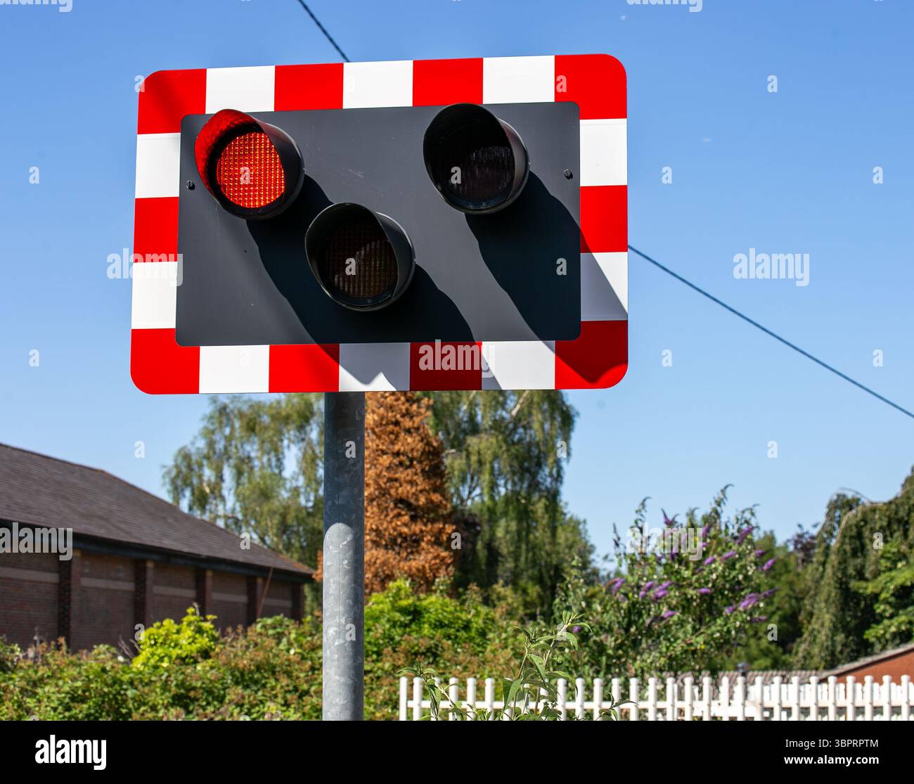 Un segnale di attraversamento ferroviario con motivo a scacchiera rosso e bianco sotto il cielo azzurro, in un ambiente rurale, stazione di Hungerford, Berkshire, Regno Unito Foto Stock