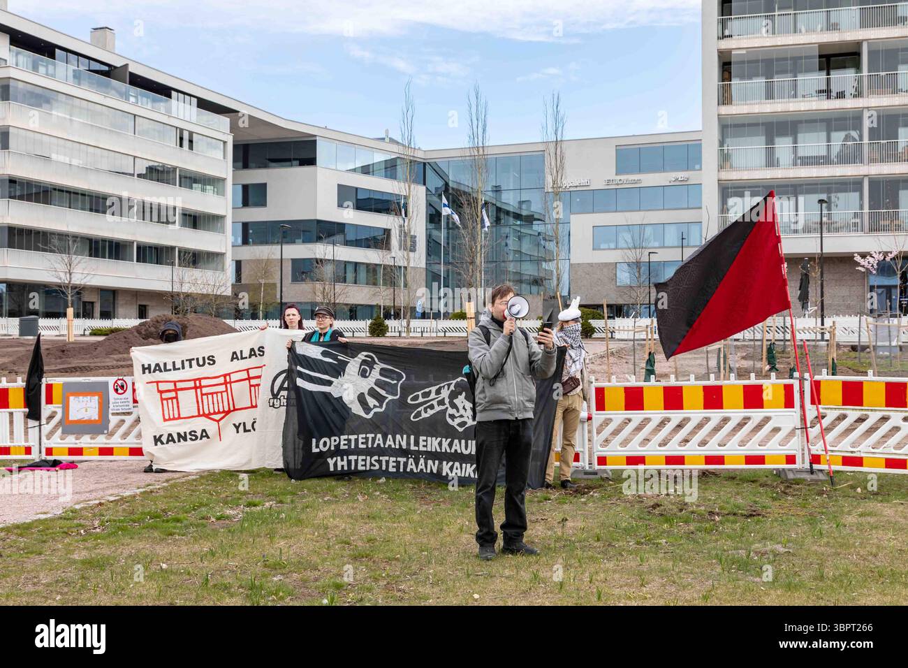 Oratore anarchico con megafono alla protesta del Labor Day. Bandiera nera e rossa e striscioni sullo sfondo. Töölönlahdenpuisto, Helsinki, Finlandia. Foto Stock