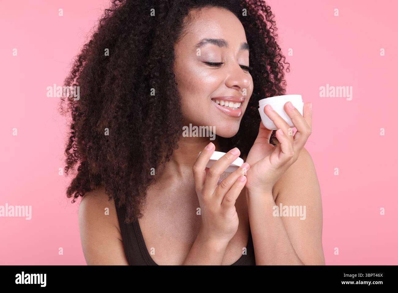 Bella donna brasiliana con barattolo di crema di collagene su sfondo rosa Foto Stock