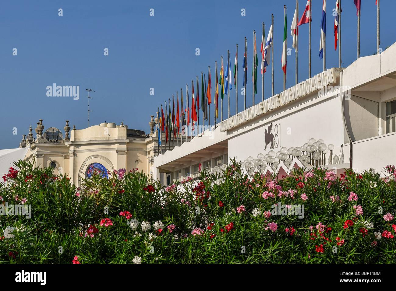 Sezione alta del Palazzo del Cinema, sede della 81a Mostra Internazionale d'Arte cinematografica di Venezia, con oleandri in fiore in primo piano, Lido di Venezia, Italia Foto Stock