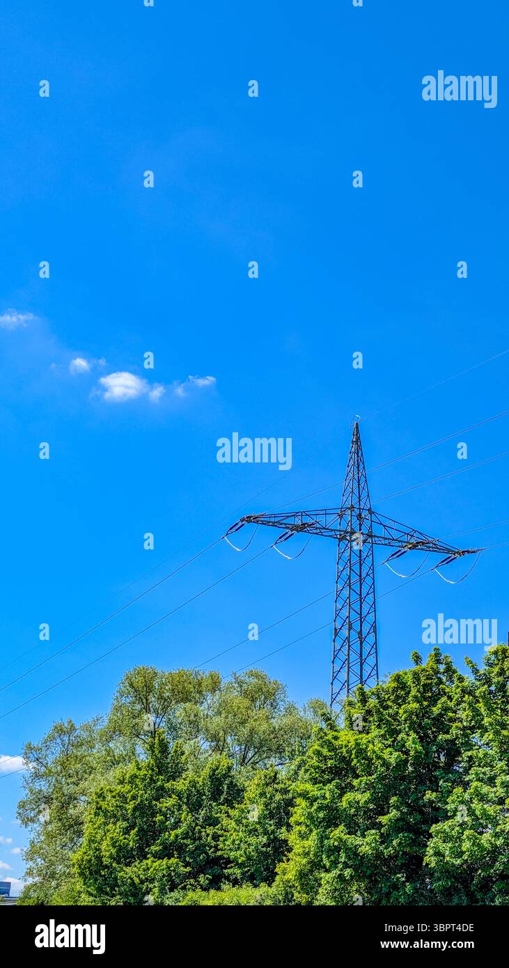 La torre di trasmissione dell'energia elettrica si erge sopra alberi verdi in una giornata di sole limpido con un cielo blu brillante. Foto Stock