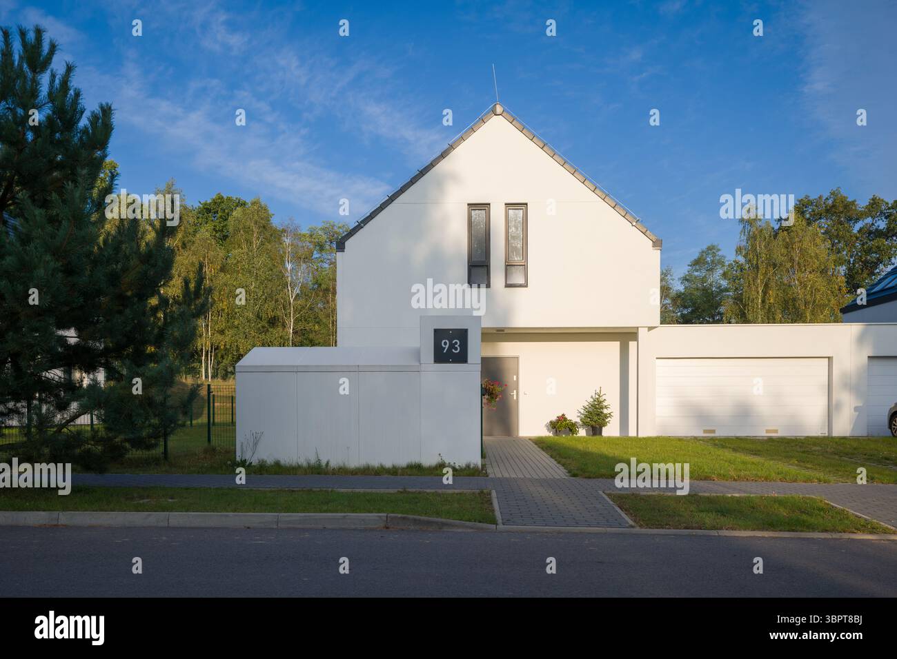 Esterno di una moderna casa unifamiliare con una facciata bianca minimalista e un garage annesso. L'albergo si trova in un tranquillo quartiere periferico Foto Stock