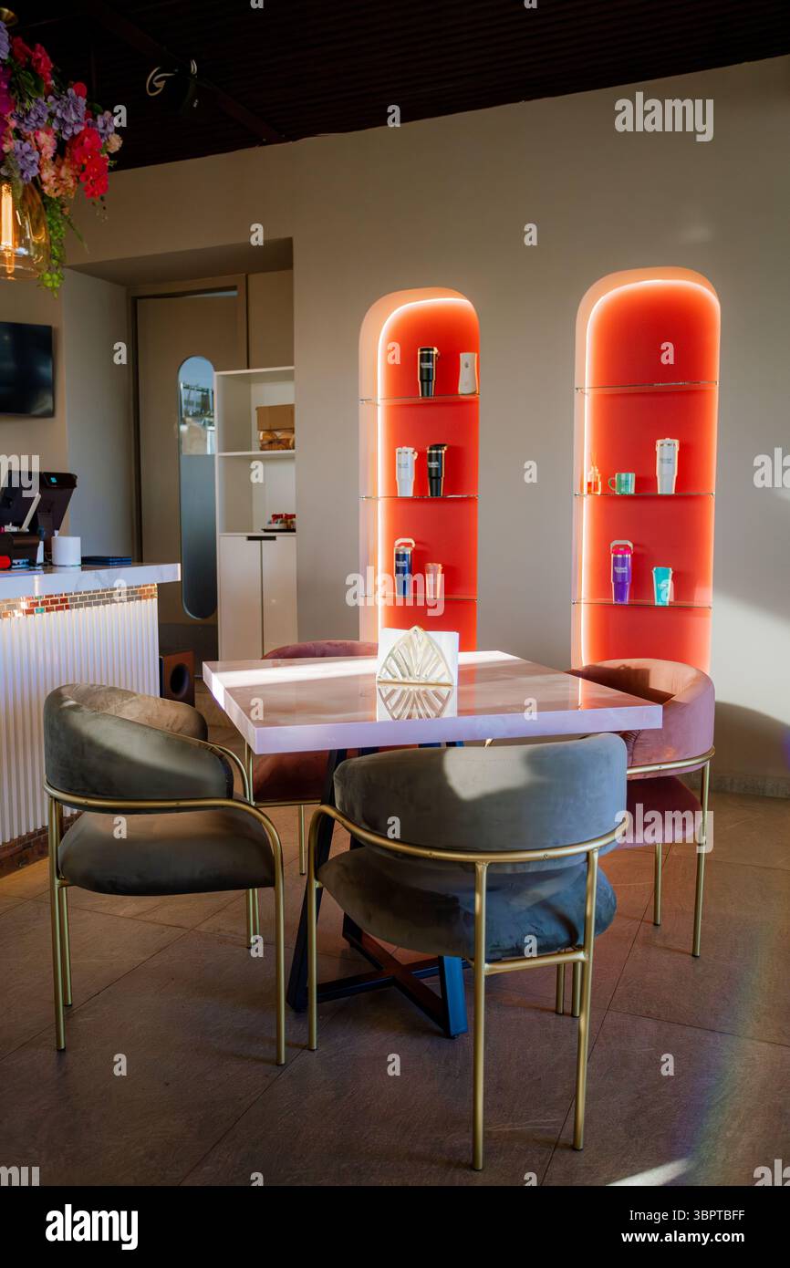 12 luglio 2025. Angolo moderno e accogliente con tavolo in marmo rosa, sedie in velluto e ripiani ad arco rossi con illuminazione a LED, ideale per una boutique Foto Stock